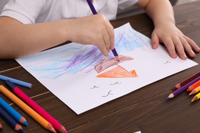 Little boy drawing ship with pencil at wooden table, closeup. Child`s art