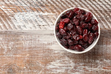 Photo of Tasty dried cranberries in bowl on rustic wooden table, top view. Space for text