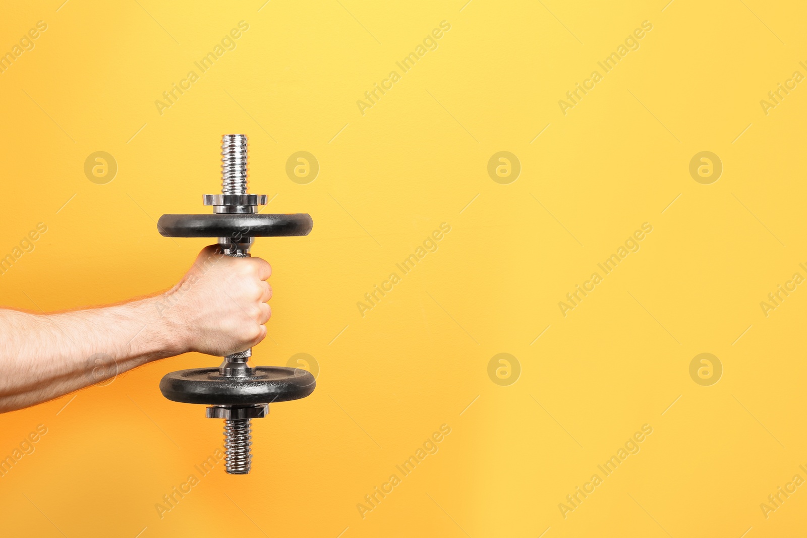 Photo of Male athlete holding metal dumbbell on color background. Space for text