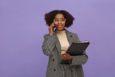 African American intern with folders talking on smartphone against purple background. Space for text