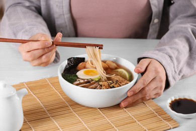 Woman eating delicious ramen with chopsticks at white table, closeup. Noodle soup