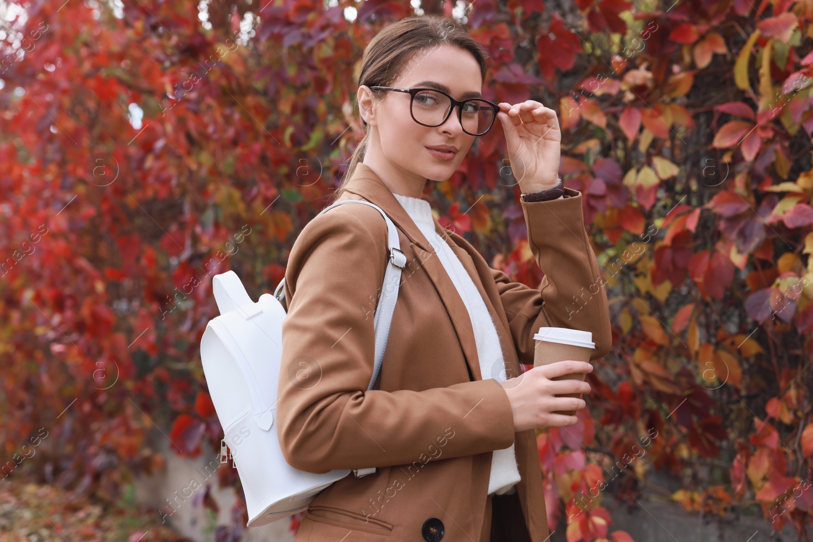 Photo of Beautiful young woman with stylish white backpack and hot drink in autumn park