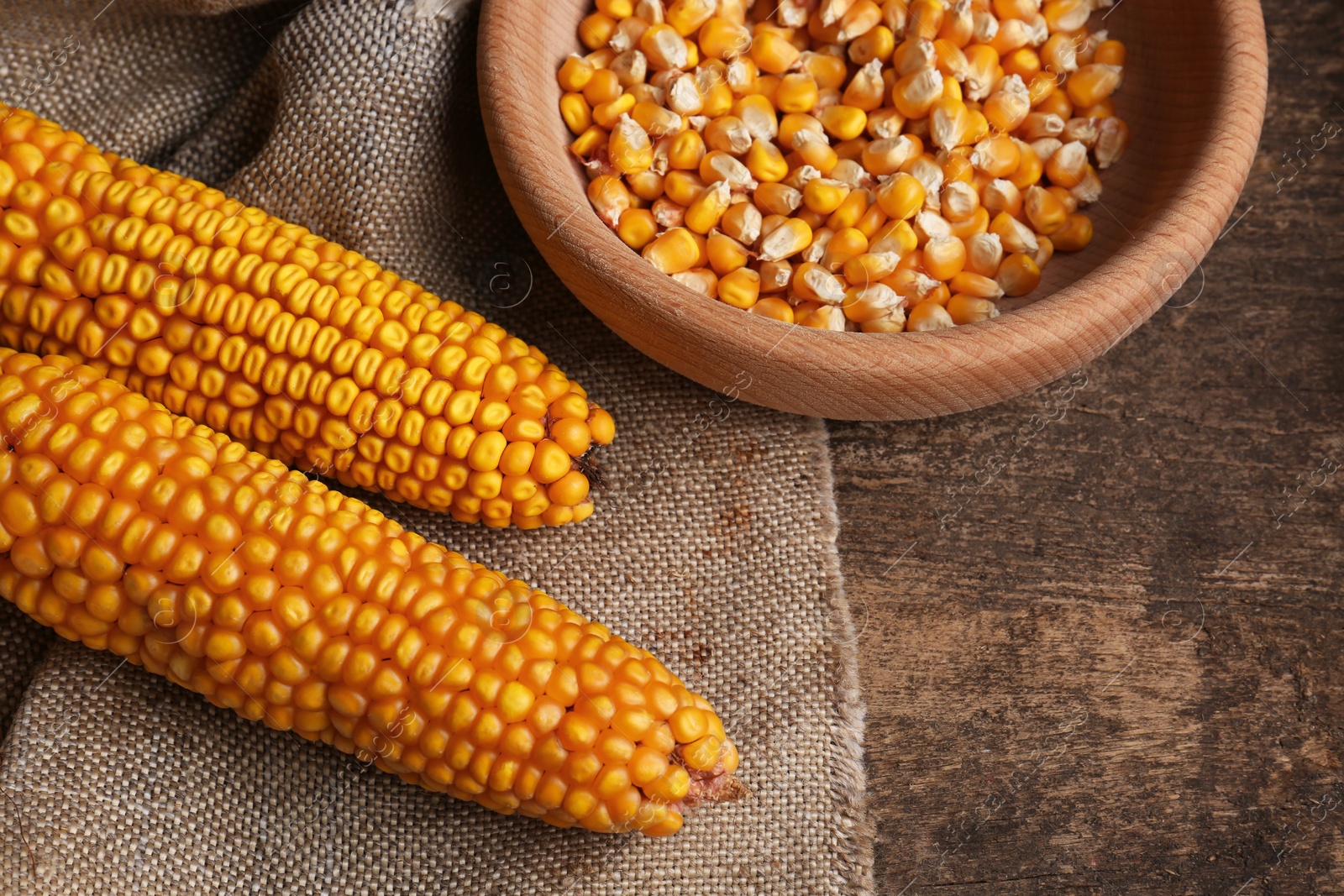 Photo of Delicious ripe corn cobs and bowl with seeds on wooden table