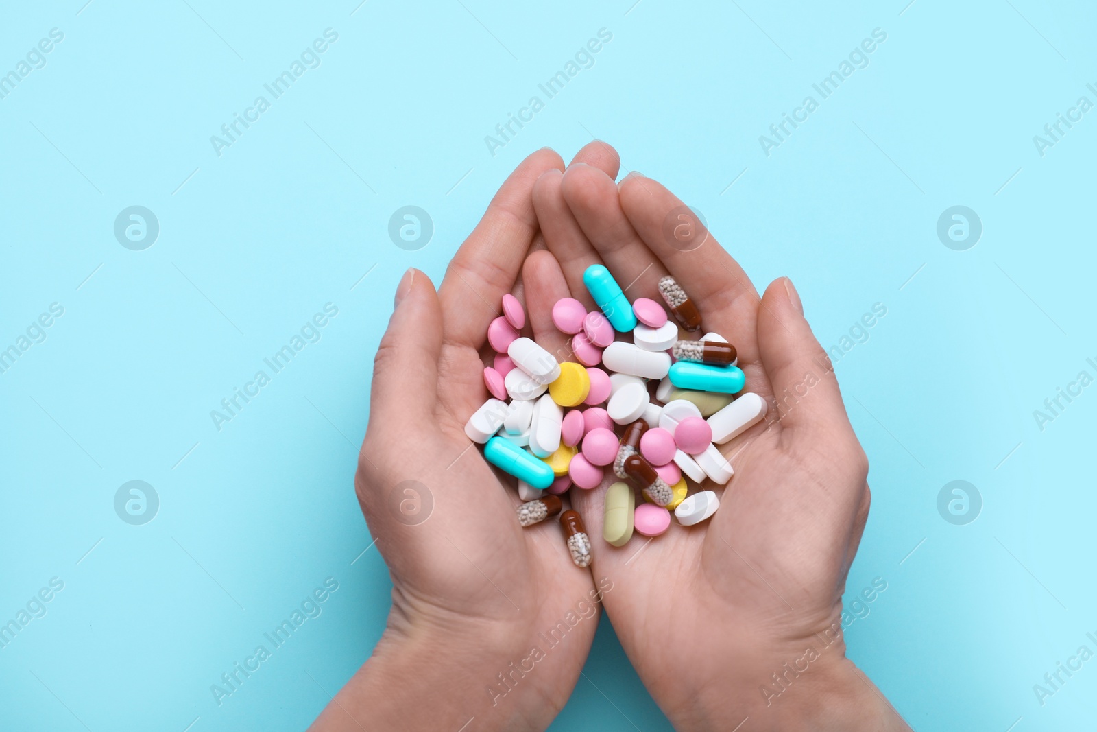 Photo of Woman holding colorful antidepressants on light blue background, top view