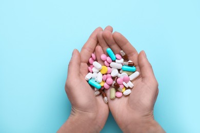 Photo of Woman holding colorful antidepressants on light blue background, top view