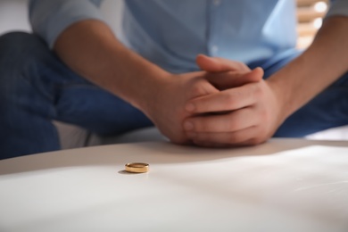 Man with wedding ring at white table, closeup. Divorce concept