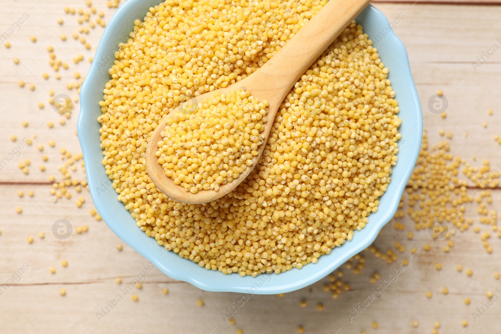 Photo of Millet groats in bowl and spoon on light wooden table, top view