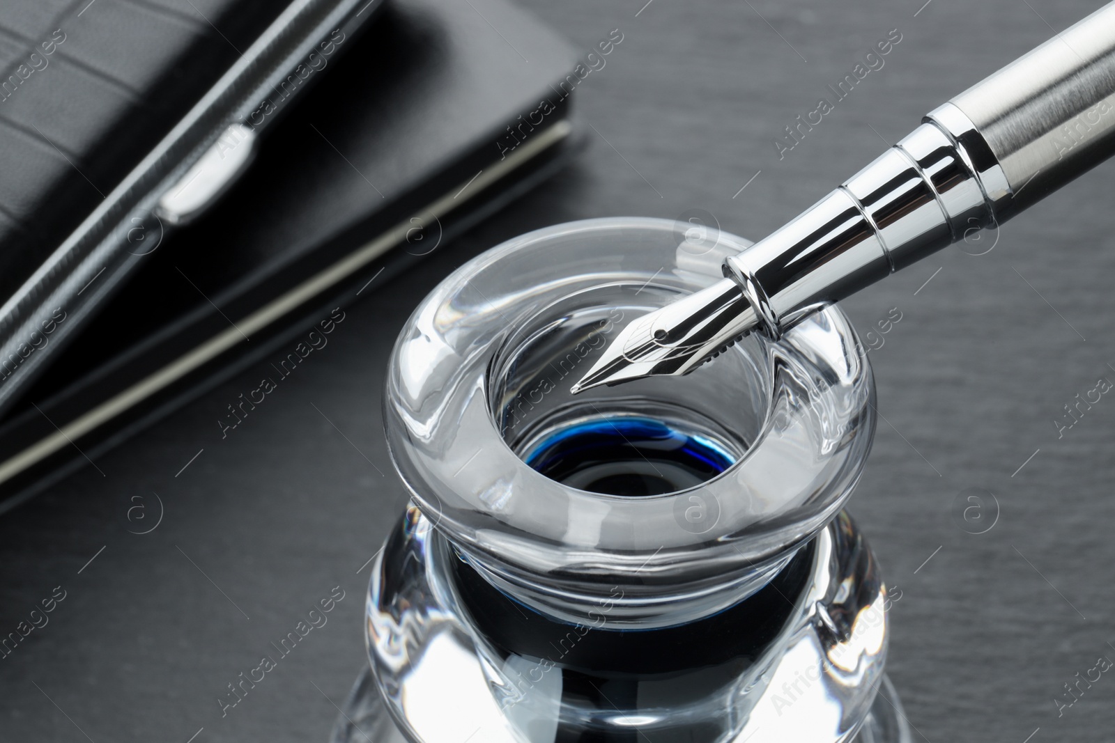 Photo of Inkwell with fountain pen on grey table, closeup