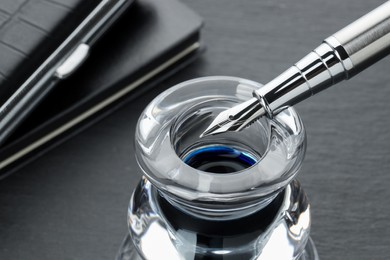 Inkwell with fountain pen on grey table, closeup