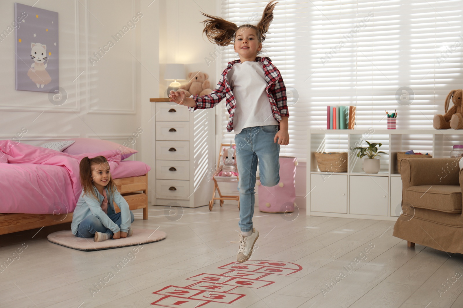 Photo of Cute little girls playing hopscotch at home