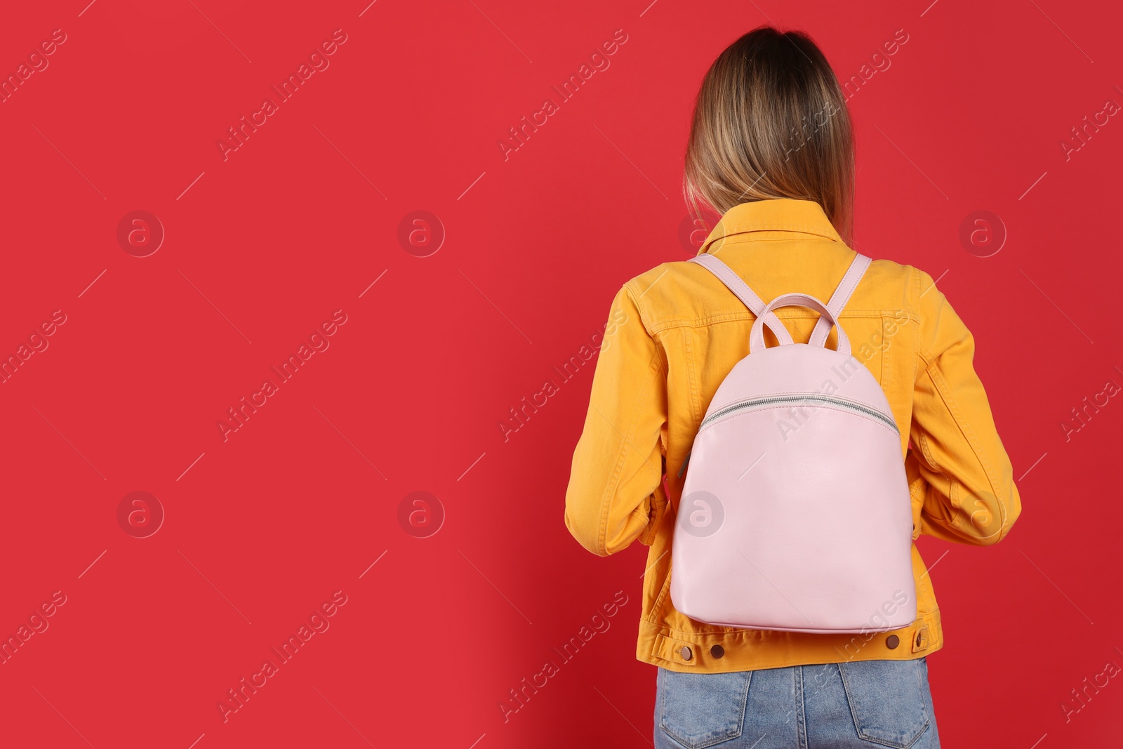 Photo of Woman with backpack on red background, back view. Space for text