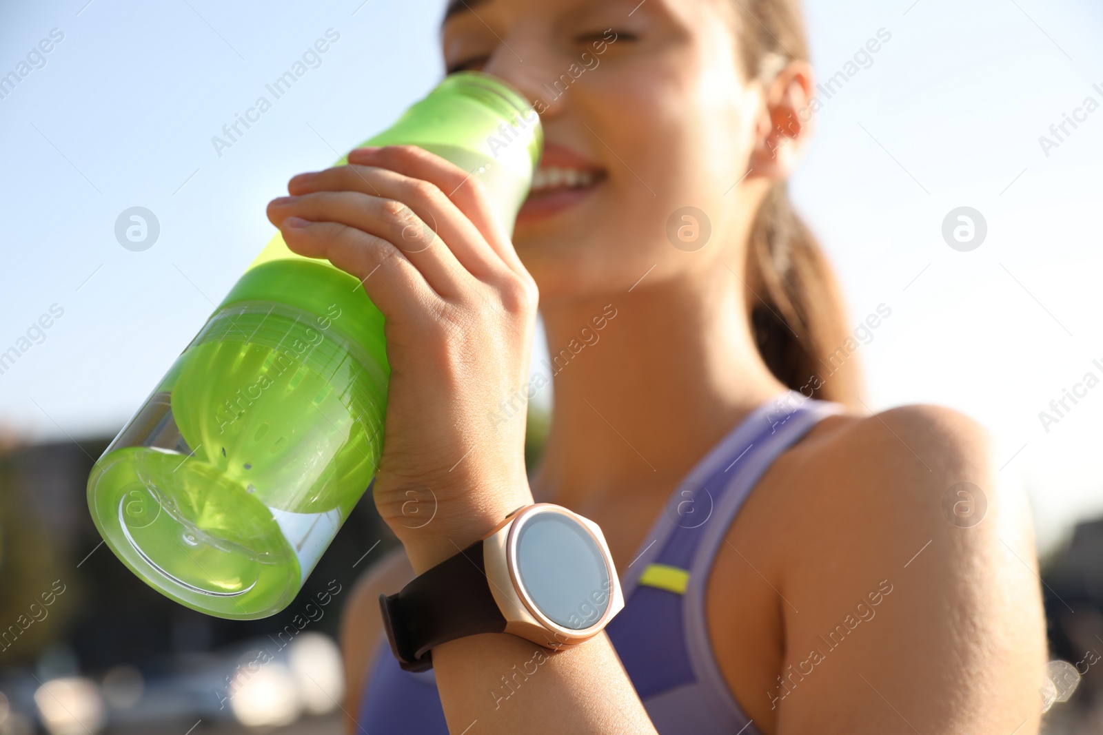 Photo of Woman with fitness tracker drinking water after training outdoors, closeup