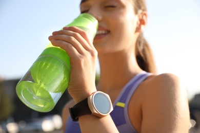 Photo of Woman with fitness tracker drinking water after training outdoors, closeup