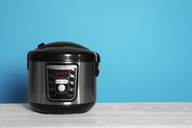 Photo of Modern electric multi cooker on table against color background. Space for text