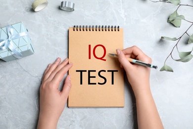 Image of IQ Test. Woman with pen and notebook at grey table, top view