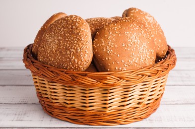 Photo of Wicker basket of fresh buns with sesame seeds on white wooden table