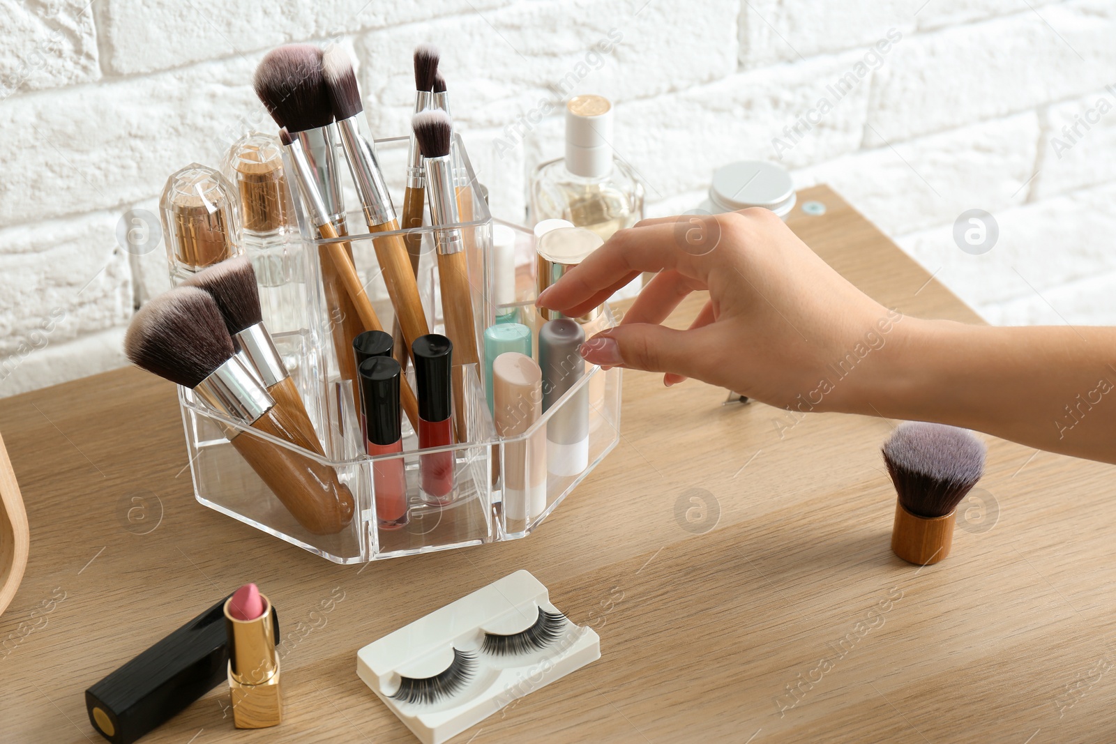 Photo of Woman taking cosmetics from organizer for makeup products on table