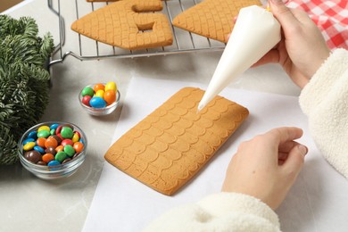 Woman making gingerbread house at light grey marble table, closeup