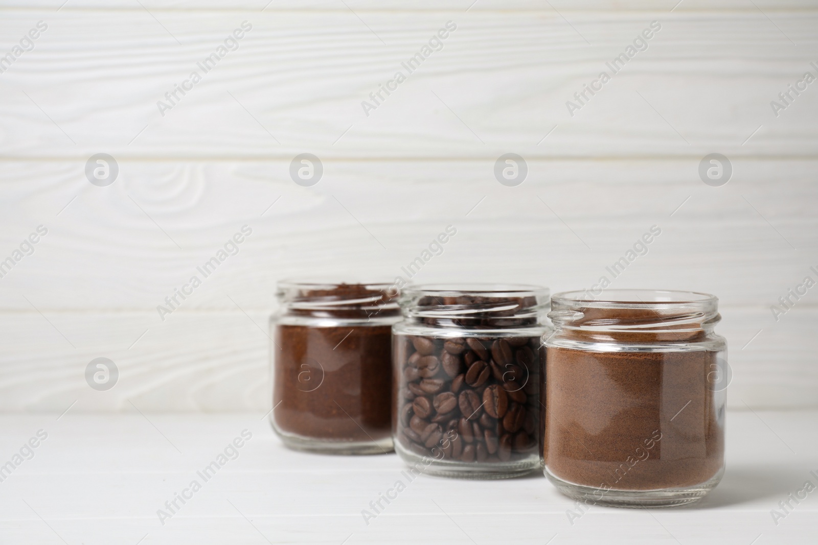 Photo of Jars with instant, ground coffee and roasted beans on white wooden table, space for text