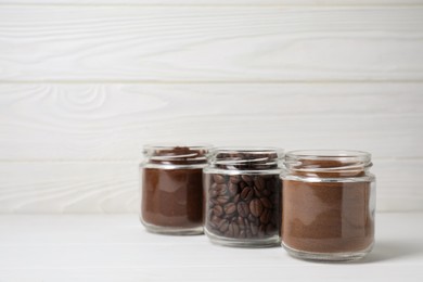 Jars with instant, ground coffee and roasted beans on white wooden table, space for text