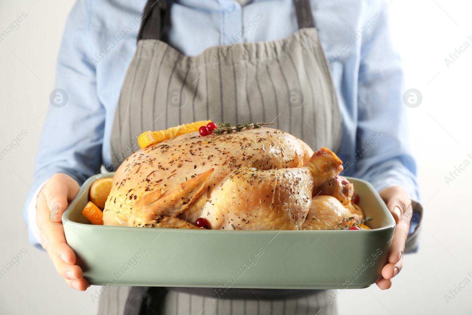 Photo of Woman holding raw chicken with orange slices on light grey background, closeup