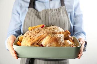 Photo of Woman holding raw chicken with orange slices on light grey background, closeup