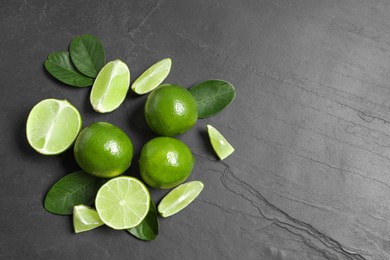 Photo of Fresh ripe limes and leaves on black table, top view. Space for text