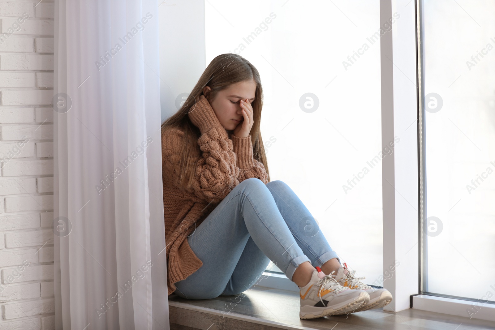 Photo of Upset teenage girl sitting alone near window indoors