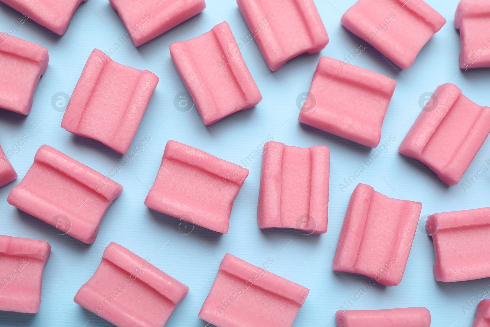 Photo of Tasty pink chewing gums on light blue background, flat lay