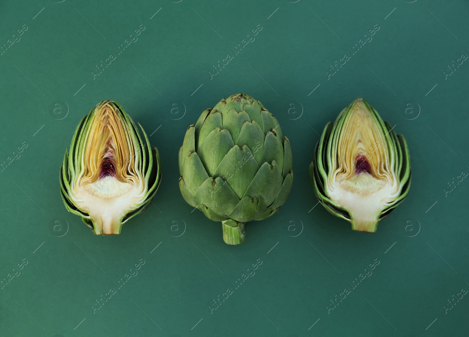 Photo of Cut and whole fresh raw artichokes on green background, flat lay