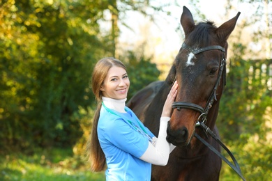 Photo of Veterinarian in uniform with beautiful brown horse outdoors. Space for text