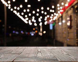 Image of Empty wooden surface and blurred view of night street decorated for Christmas. Bokeh effect