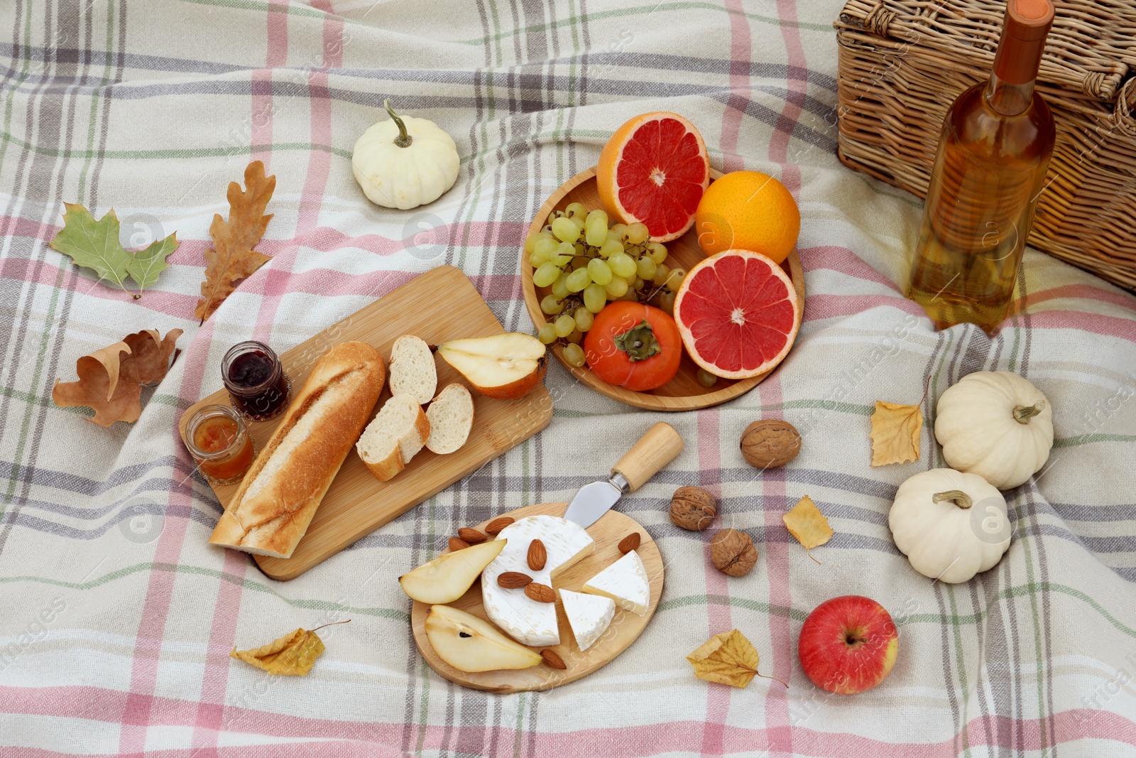 Photo of Blanket with picnic basket, wine, snacks and autumn leaves, above view