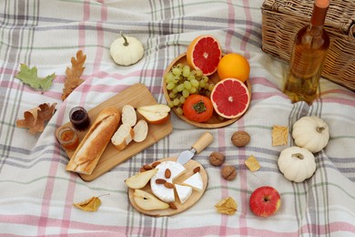 Blanket with picnic basket, wine, snacks and autumn leaves, above view