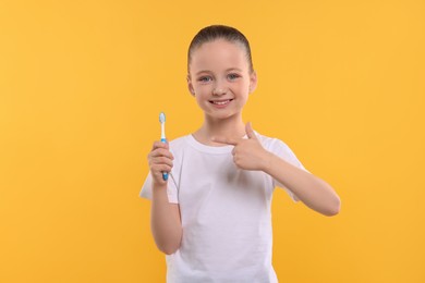 Happy girl holding toothbrush on yellow background