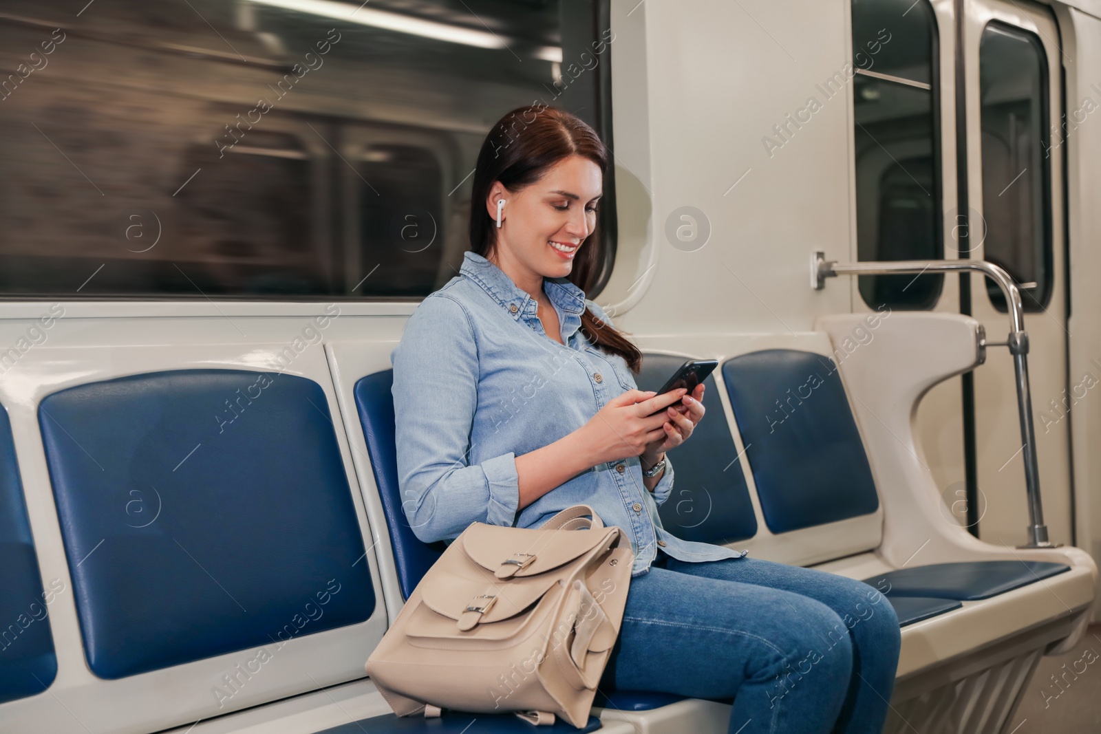 Photo of Beautiful woman with mobile phone and earbuds listening to music in subway train. Public transport