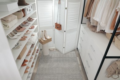 Photo of Dressing room interior with clothes rack and collection of stylish shoes, above view