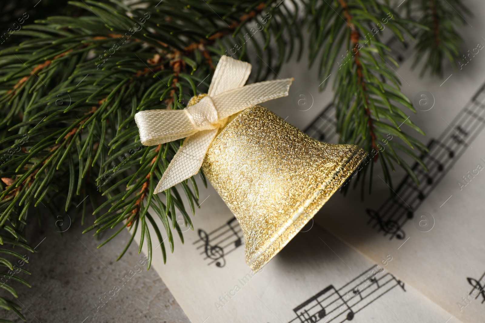 Photo of Golden shiny bell with bow, music sheets and fir branches on light table. top view. Christmas decoration