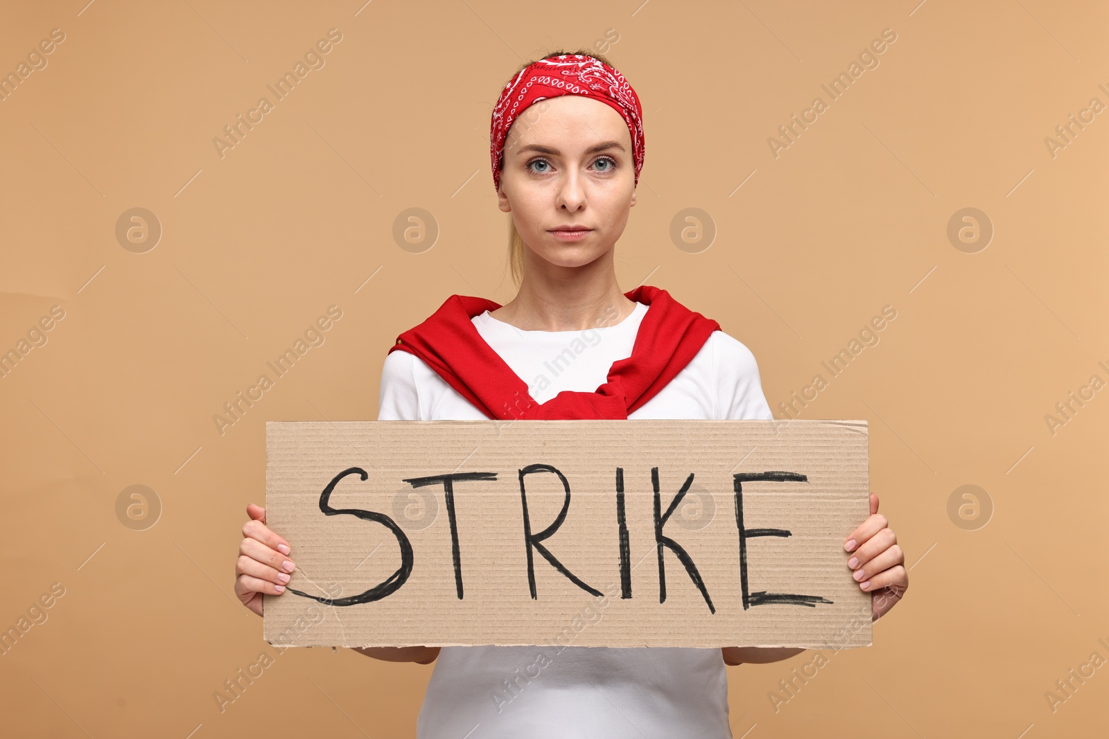 Photo of Beautiful woman holding cardboard banner with word Strike on beige background