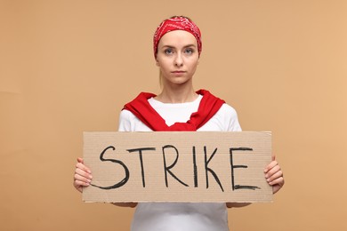 Photo of Beautiful woman holding cardboard banner with word Strike on beige background