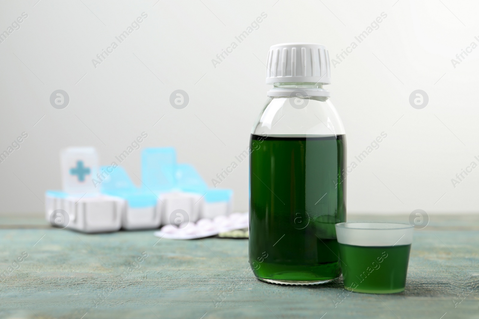 Photo of Bottle of syrup and measuring cup on wooden table against white background, space for text. Cold medicine
