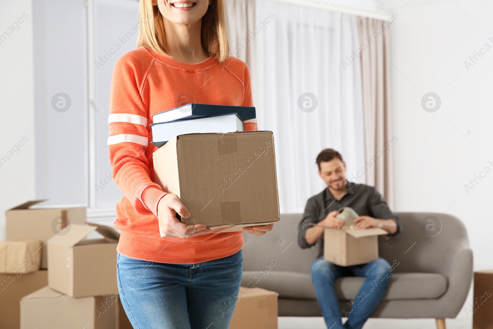 Photo of Woman carrying box full of books while man unpacking other in new house. Moving day