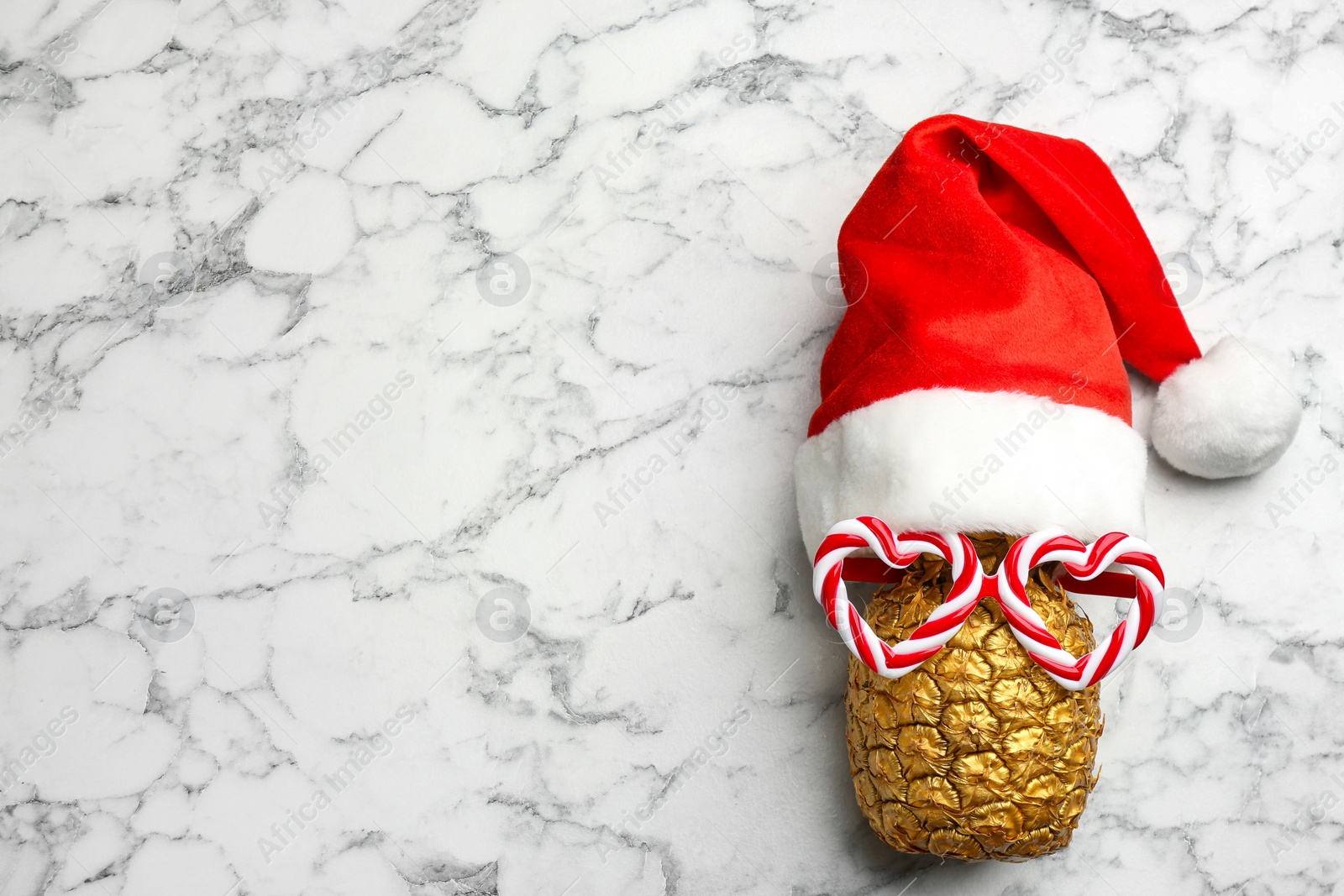 Photo of Top view of pineapple with funny glasses and Santa hat on white marble background, space for text. Creative concept