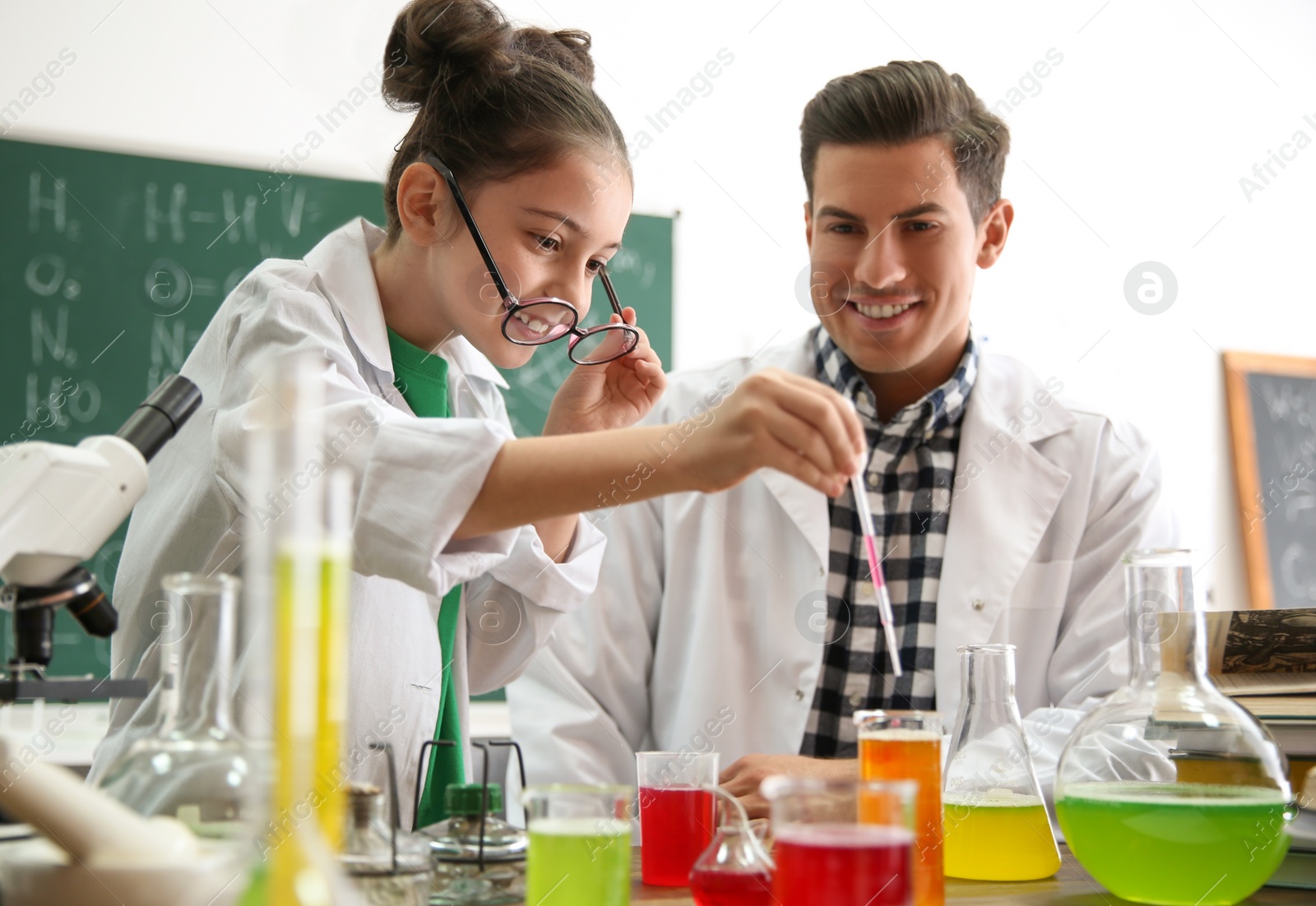 Photo of Teacher with pupil making experiment at table in chemistry class