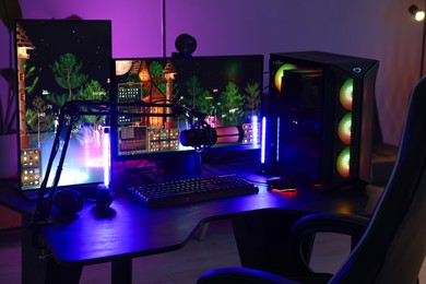 Photo of Playing video games. Stylish room interior with modern computer and gaming chair in neon lights