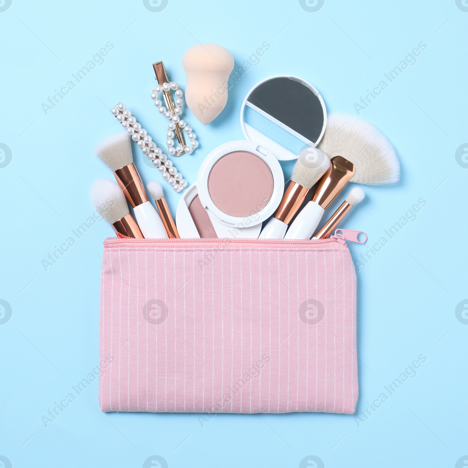 Photo of Cosmetic bag with makeup products and beauty accessories on light blue background, flat lay