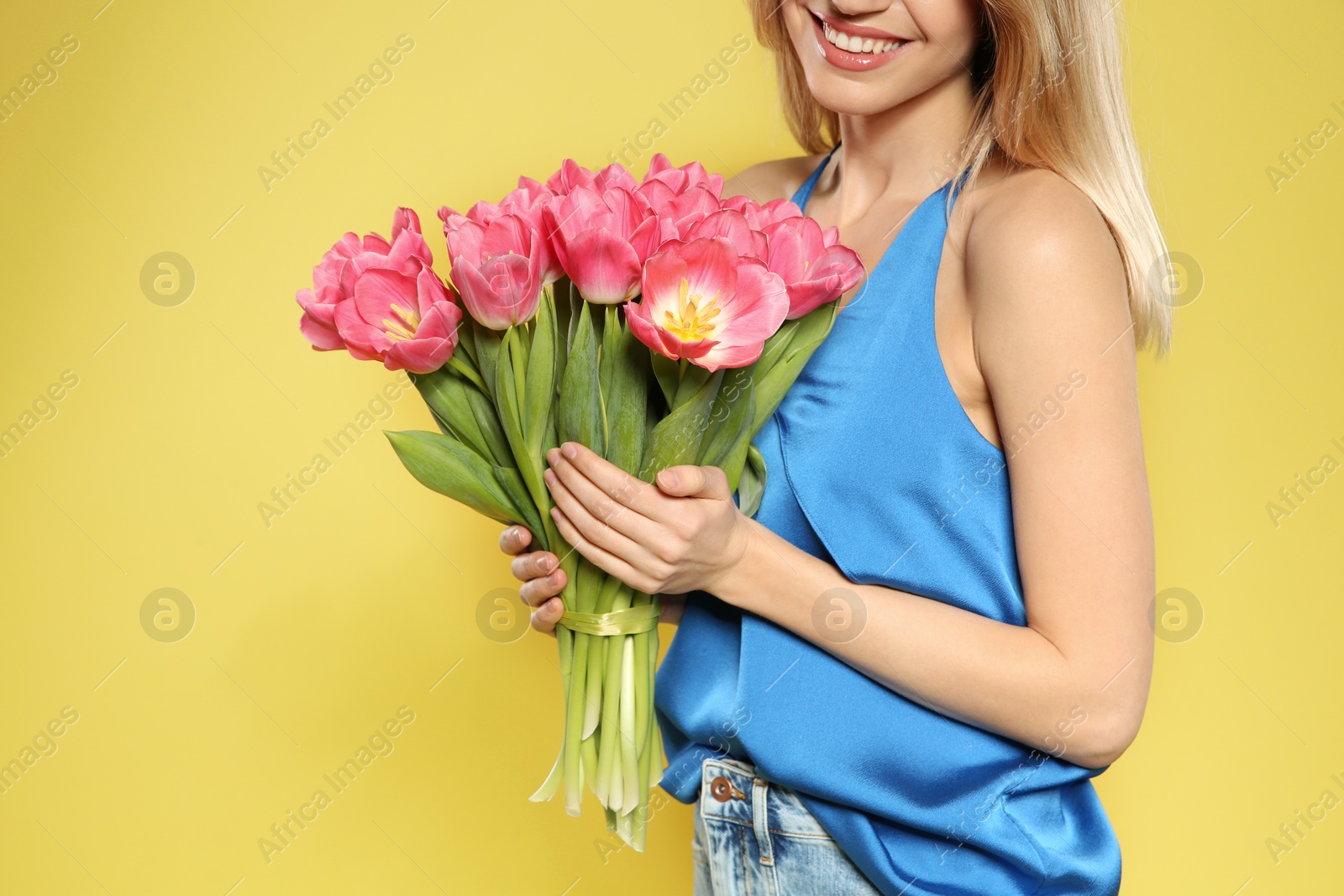 Photo of Beautiful girl with spring tulips on yellow background, closeup. International Women's Day