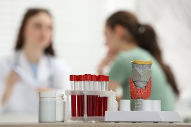 Photo of Endocrinologist examining patient at clinic, focus on model of thyroid gland, pills and blood samples in test tubes