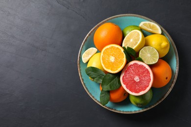 Photo of Different cut and whole citrus fruits on black table, top view. Space for text