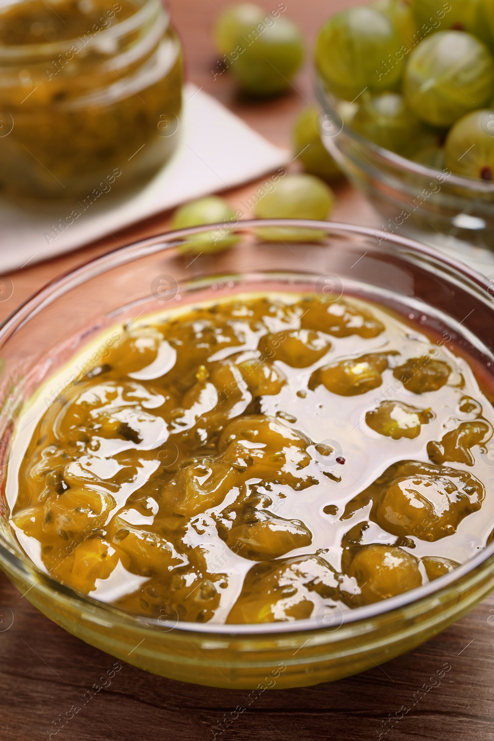 Photo of Bowl of delicious gooseberry jam and fresh berries on wooden table, closeup